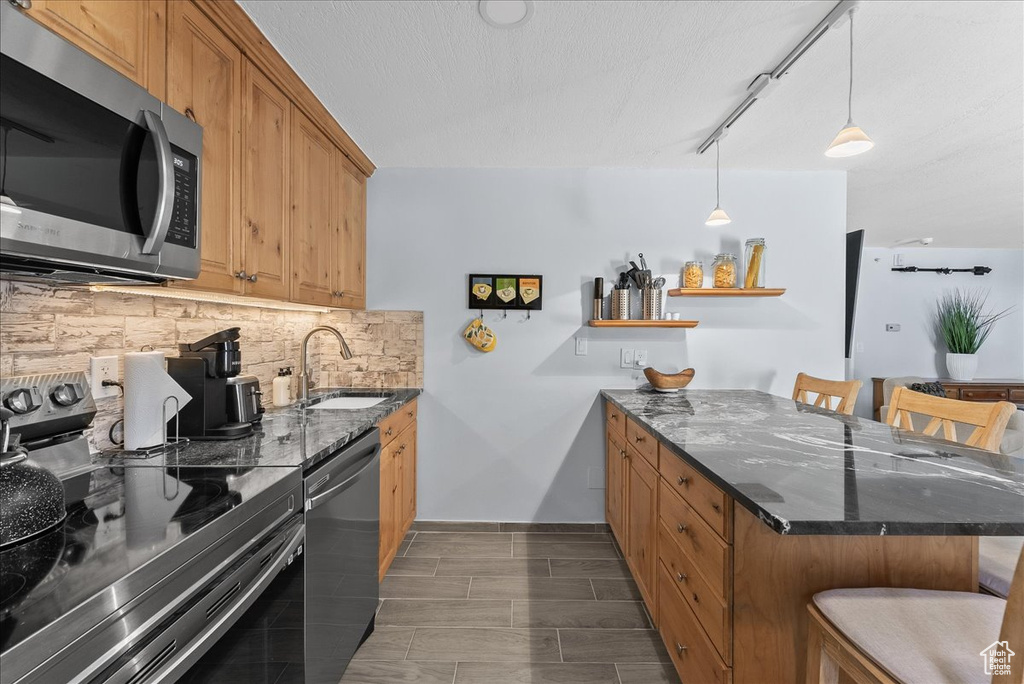 Kitchen featuring a kitchen breakfast bar, sink, hanging light fixtures, and stainless steel appliances