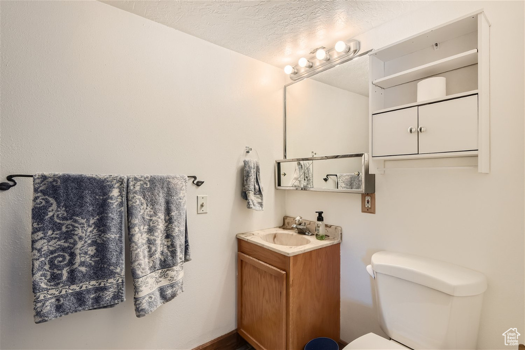Bathroom featuring toilet, vanity with extensive cabinet space, and a textured ceiling