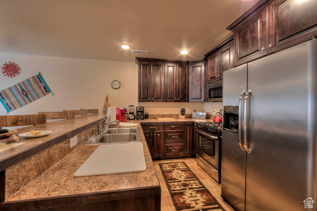 Kitchen featuring dark brown cabinets, light tile flooring, sink, and appliances with stainless steel finishes