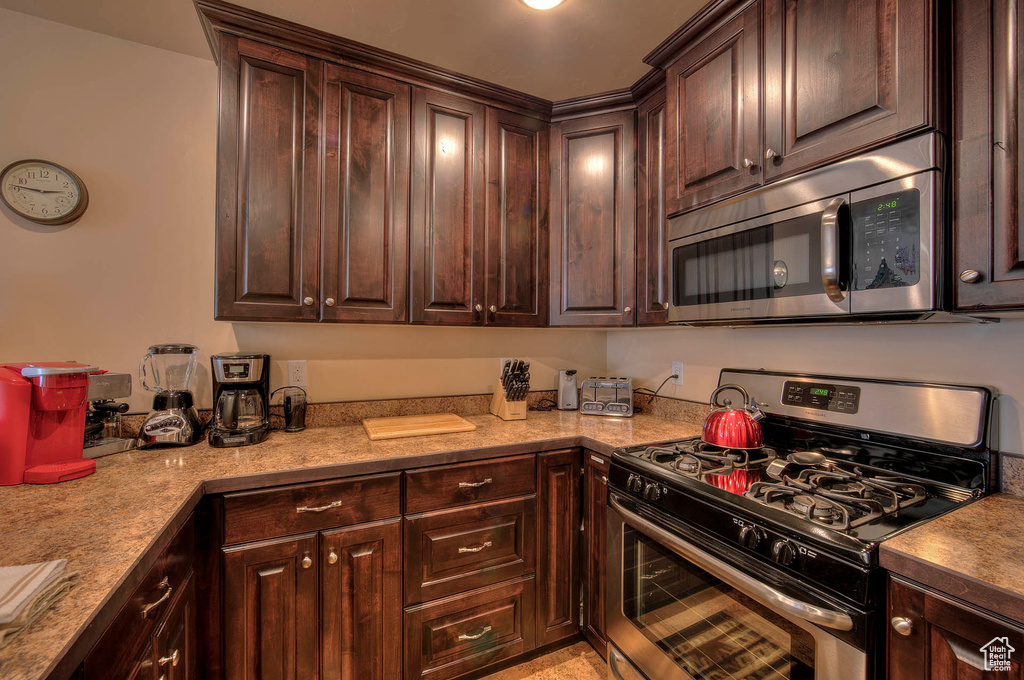 Kitchen with dark brown cabinetry, stainless steel appliances, and light stone counters