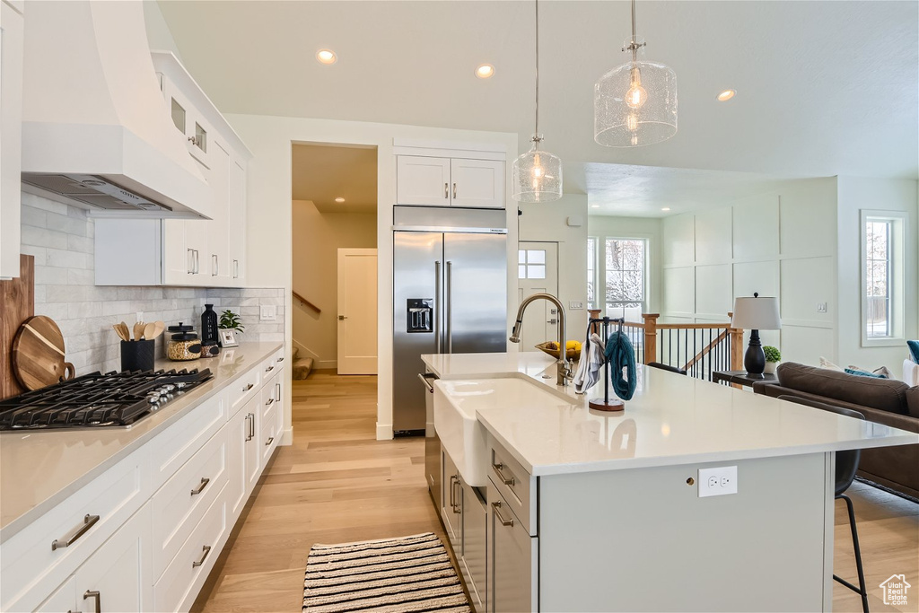 Kitchen featuring light hardwood / wood-style floors, tasteful backsplash, a kitchen bar, custom range hood, and a kitchen island with sink