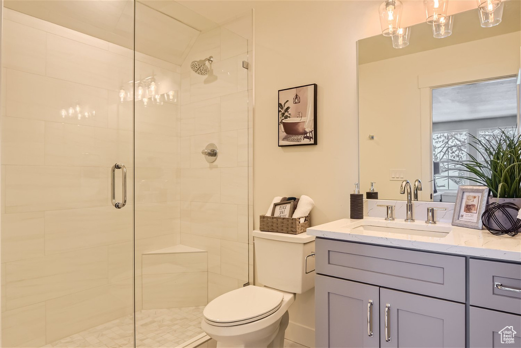 Bathroom featuring a shower with shower door, toilet, and vanity with extensive cabinet space