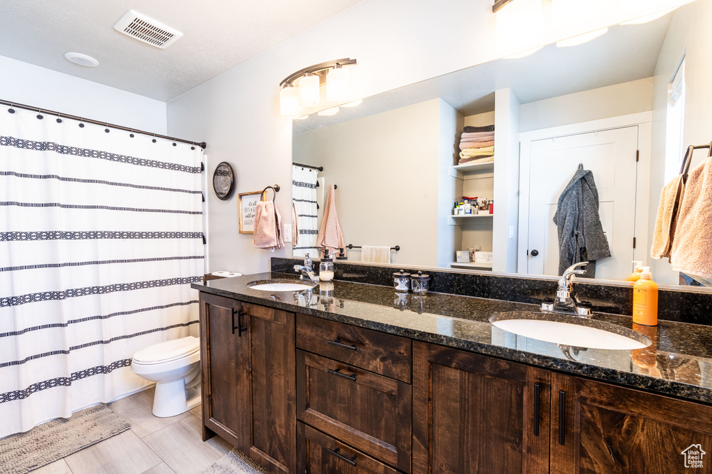 Bathroom featuring tile floors, oversized vanity, toilet, and dual sinks