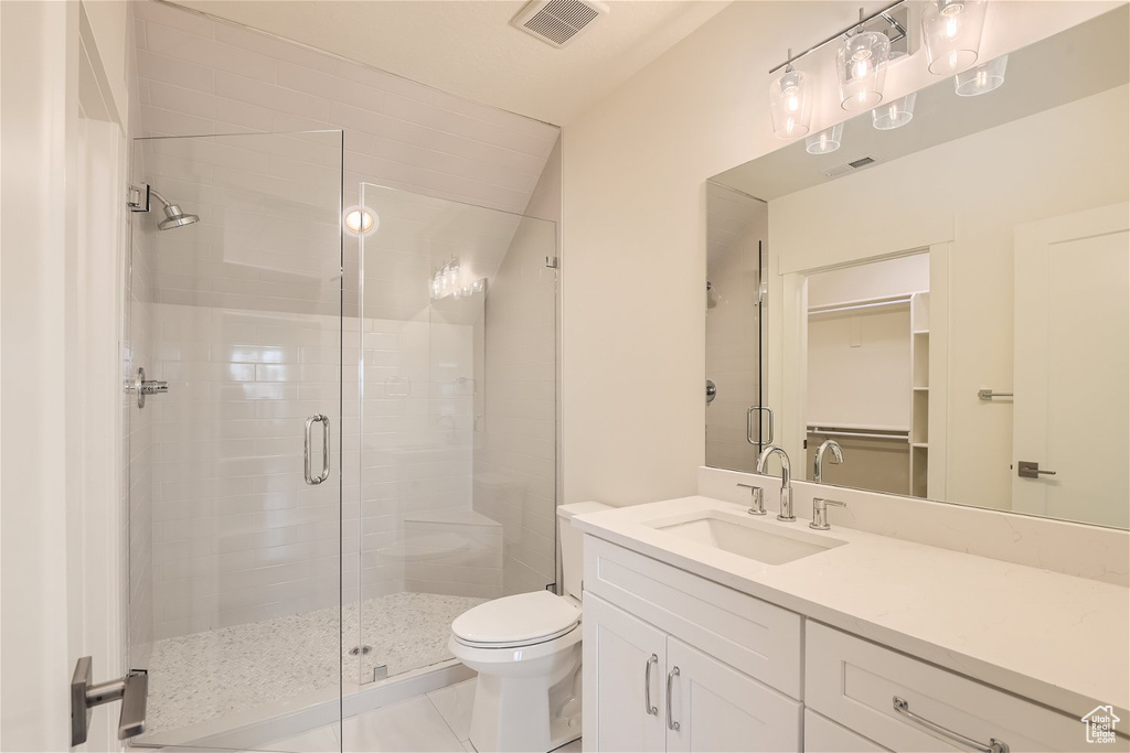 Bathroom featuring a shower with shower door, toilet, vanity, and tile floors