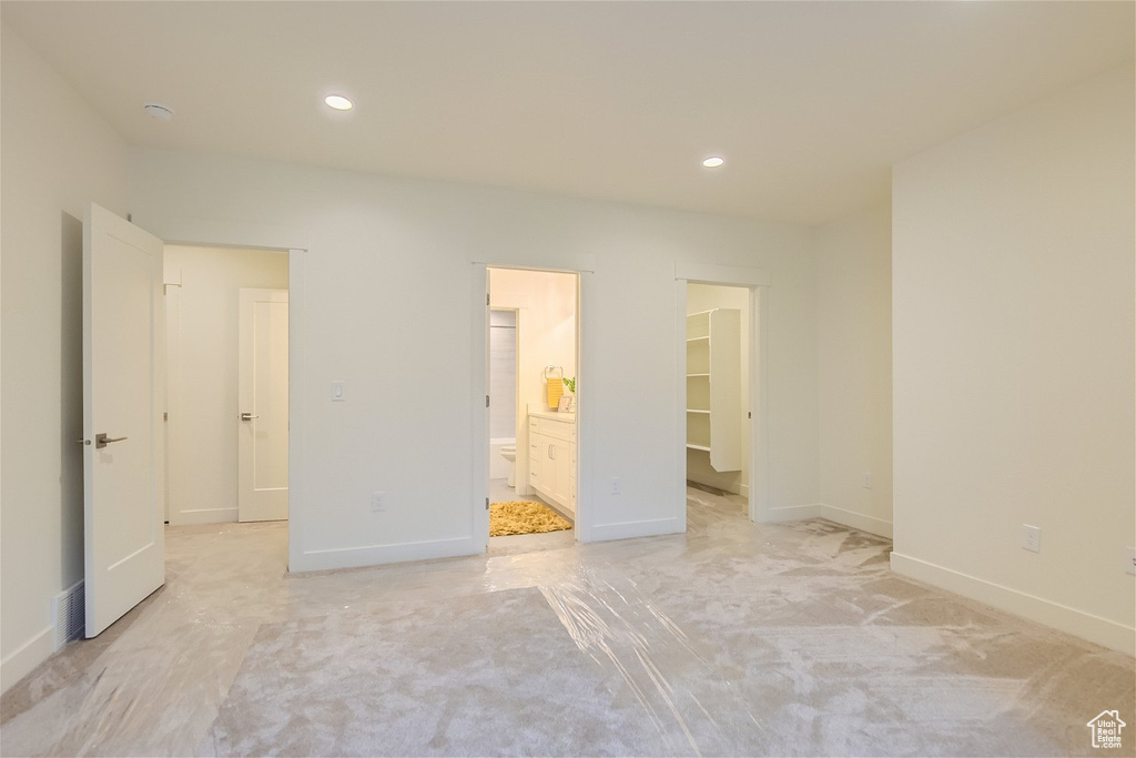 Unfurnished bedroom with light carpet, a closet, ensuite bathroom, and a walk in closet