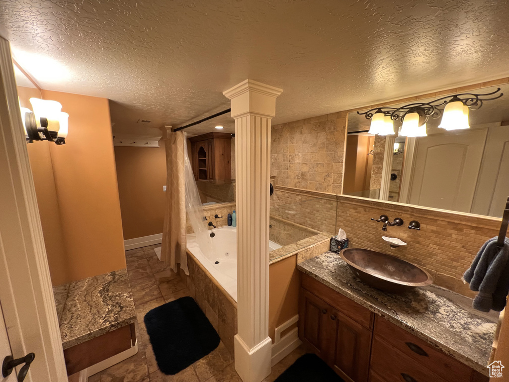 Bathroom with ornate columns, a textured ceiling, large vanity, tile floors, and tasteful backsplash