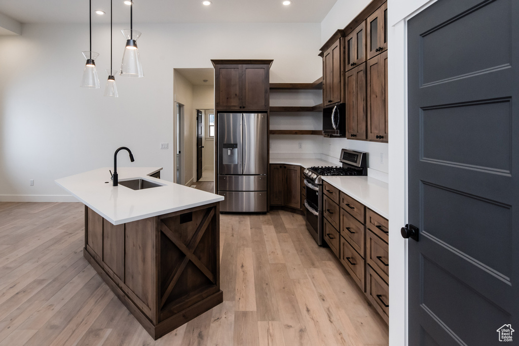 Kitchen with sink, light wood-type flooring, appliances with stainless steel finishes, and pendant lighting