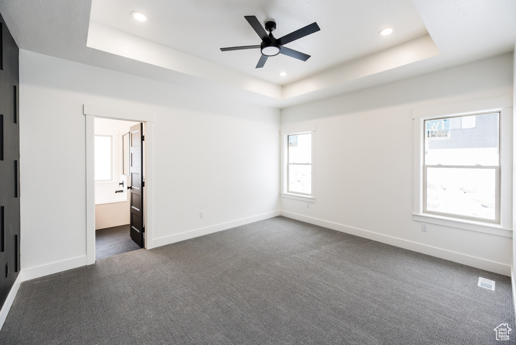 Unfurnished bedroom with ensuite bathroom, dark carpet, a tray ceiling, and ceiling fan