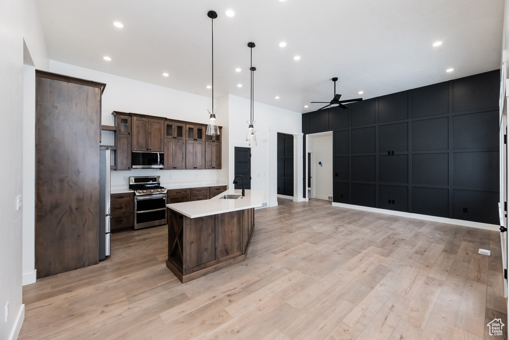 Kitchen with appliances with stainless steel finishes, pendant lighting, light hardwood / wood-style flooring, ceiling fan, and a kitchen island with sink