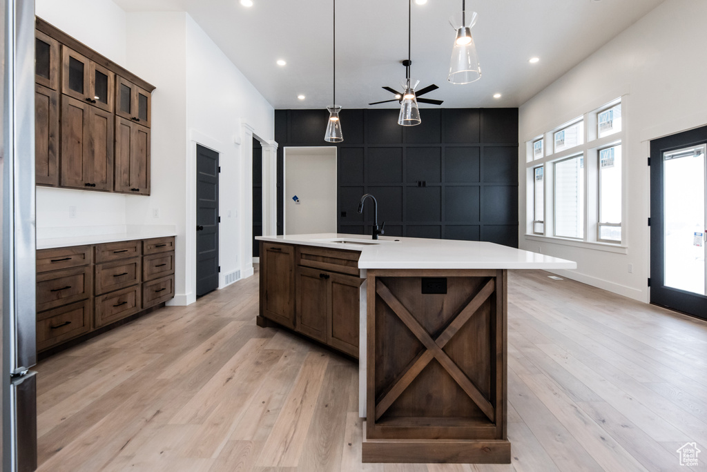 Kitchen featuring sink, light wood-type flooring, pendant lighting, and a center island with sink