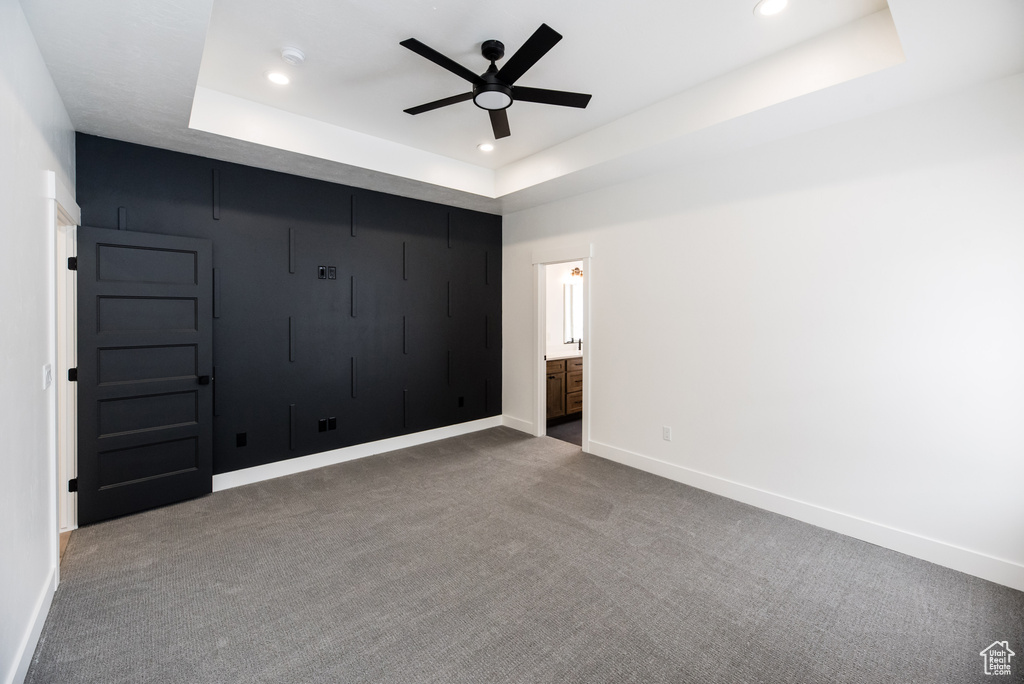 Spare room featuring ceiling fan, dark carpet, and a raised ceiling