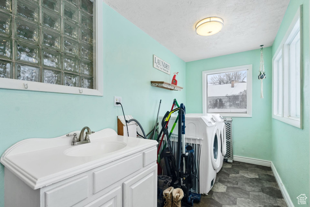 Laundry room with sink, washing machine and dryer, a textured ceiling, and dark tile floors