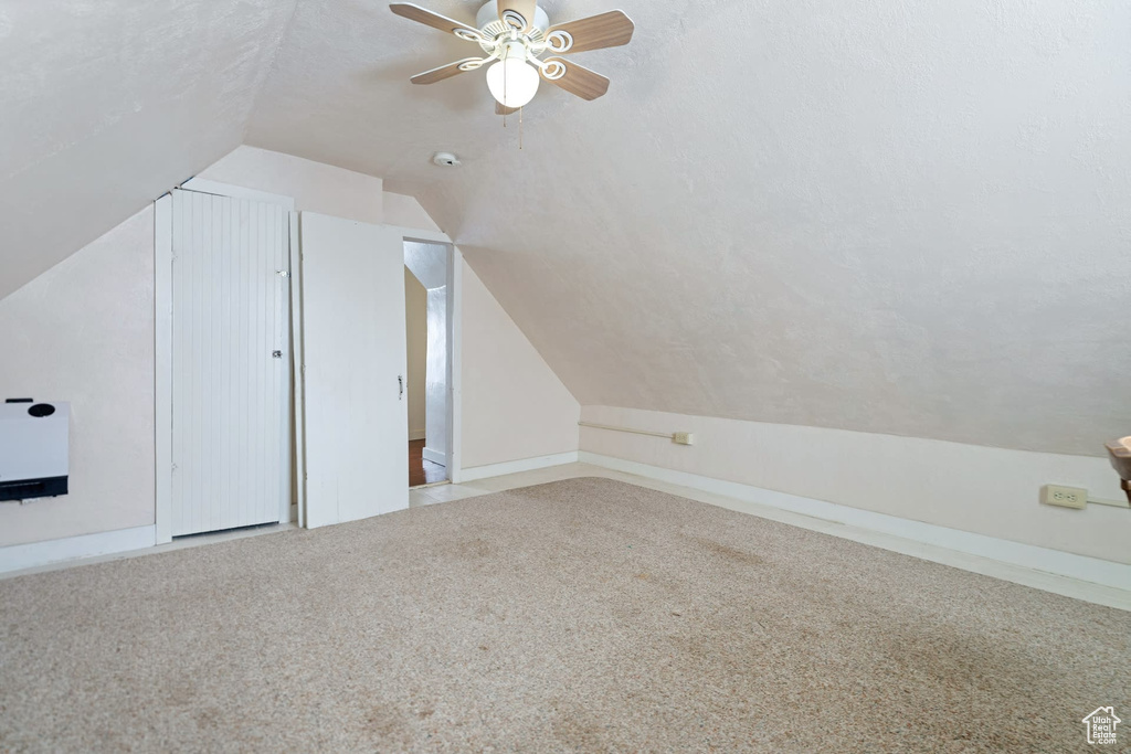 Additional living space featuring vaulted ceiling, light colored carpet, a textured ceiling, and ceiling fan