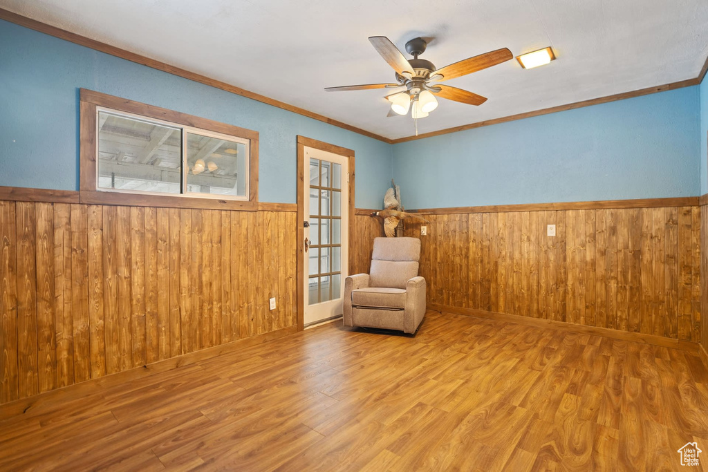 Unfurnished room with crown molding, wooden walls, light wood-type flooring, and ceiling fan