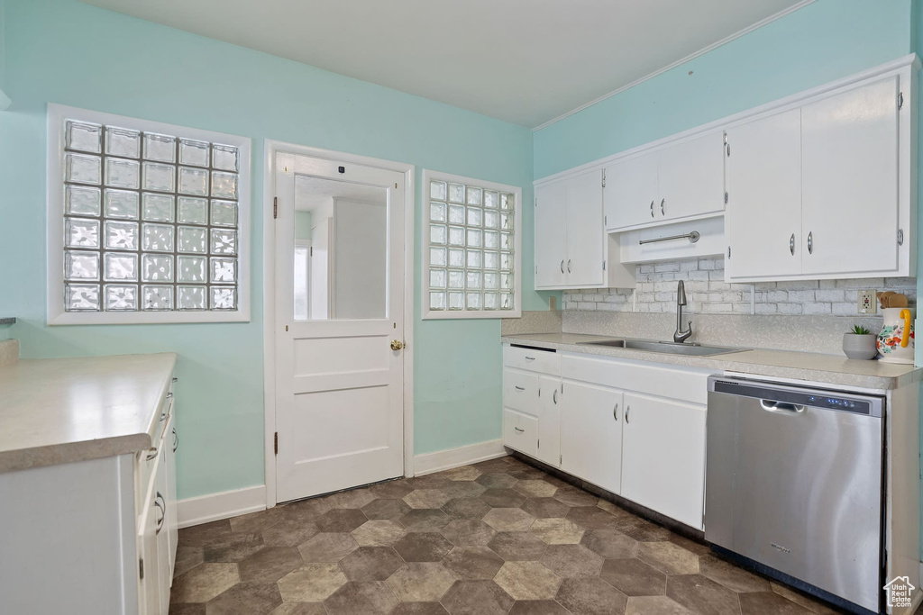 Kitchen featuring tasteful backsplash, dark tile floors, white cabinets, dishwasher, and sink