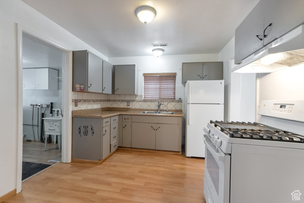 Kitchen featuring white appliances, light hardwood / wood-style flooring, gray cabinets, sink, and tasteful backsplash