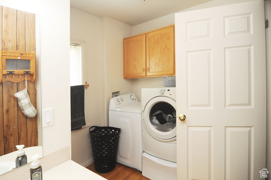 Clothes washing area featuring washer and clothes dryer, cabinets, washer hookup, and hardwood / wood-style flooring