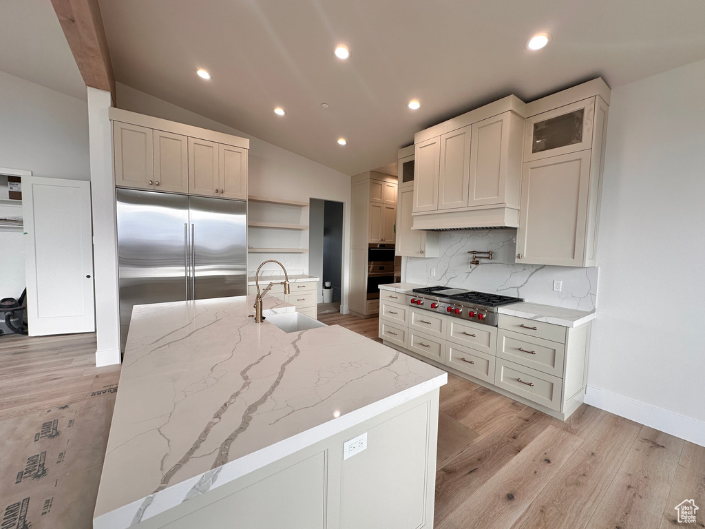 Kitchen with light stone countertops, appliances with stainless steel finishes, backsplash, light hardwood / wood-style flooring, and sink