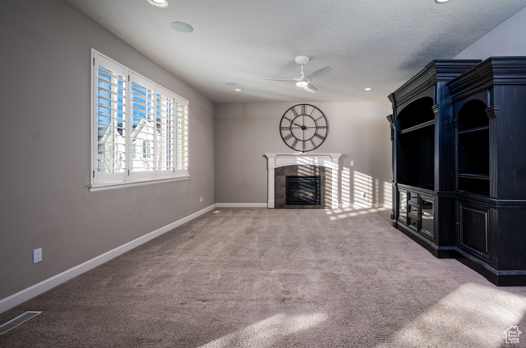 Unfurnished living room with a tile fireplace, ceiling fan, a textured ceiling, and light colored carpet