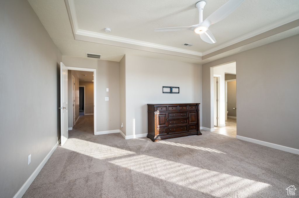 Unfurnished bedroom featuring ceiling fan, a raised ceiling, crown molding, and light carpet