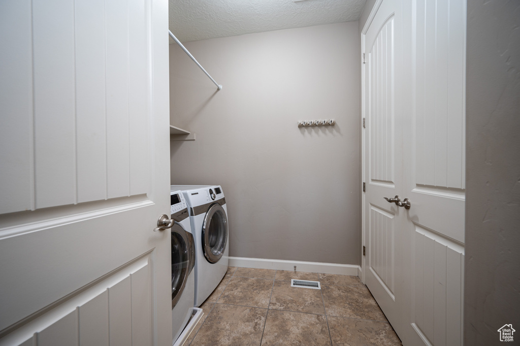 Laundry area with light tile floors, washing machine and clothes dryer, and a textured ceiling
