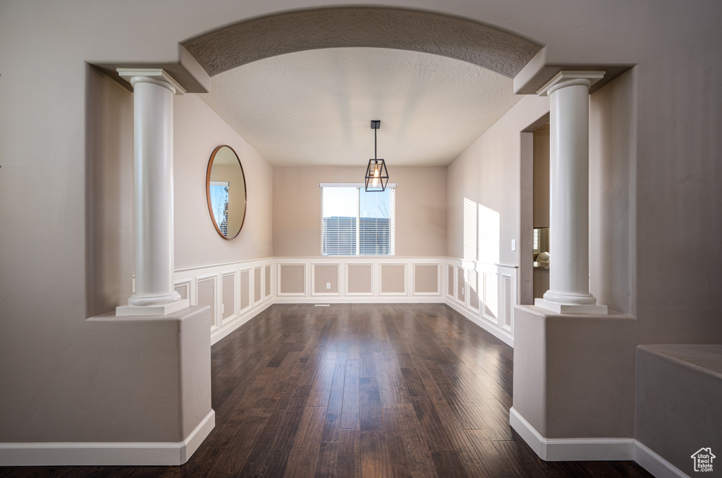 Interior space with ornate columns, a textured ceiling, and dark hardwood / wood-style flooring