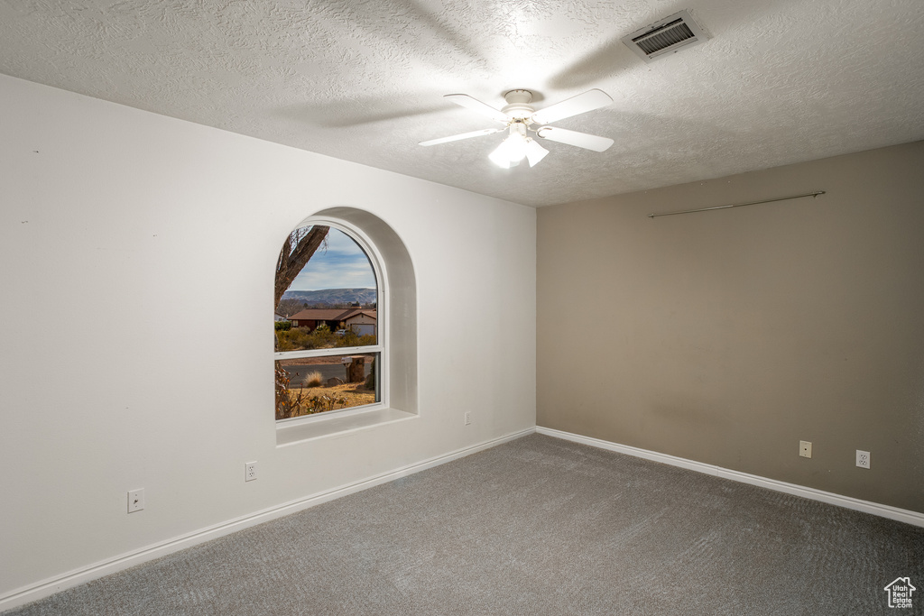 Carpeted empty room with a textured ceiling and ceiling fan