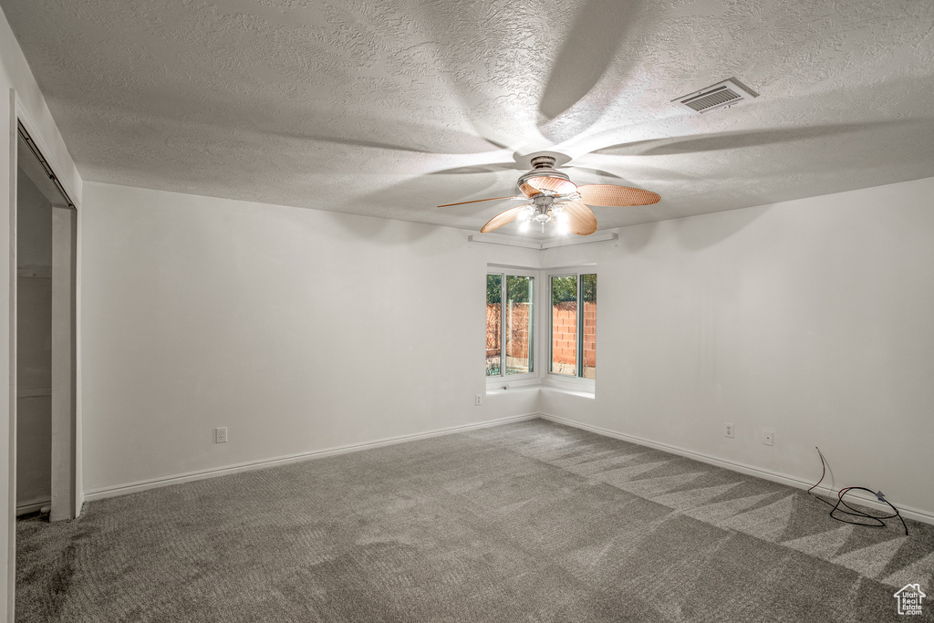 Unfurnished room with dark carpet, a textured ceiling, and ceiling fan