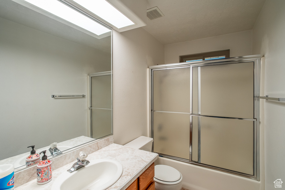 Full bathroom featuring shower / bath combination with glass door, toilet, and vanity