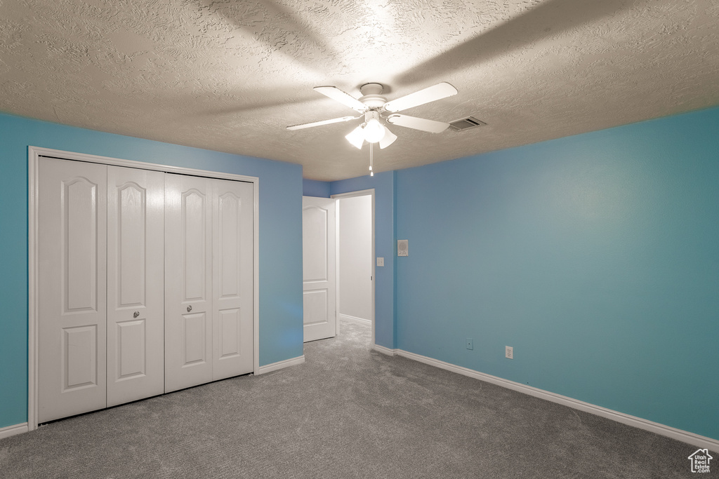 Unfurnished bedroom featuring a textured ceiling, a closet, dark colored carpet, and ceiling fan