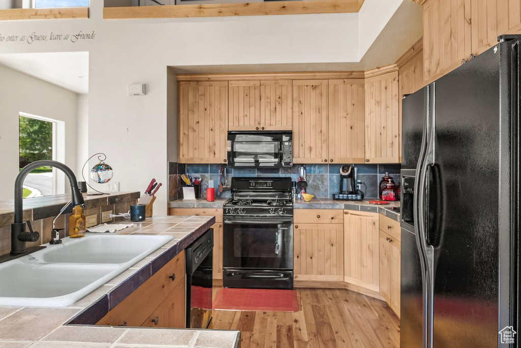 Kitchen with tile counters, tasteful backsplash, light hardwood / wood-style floors, and black appliances