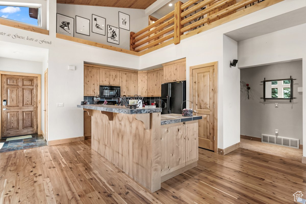 Kitchen featuring black appliances, a breakfast bar, light wood-type flooring, and high vaulted ceiling