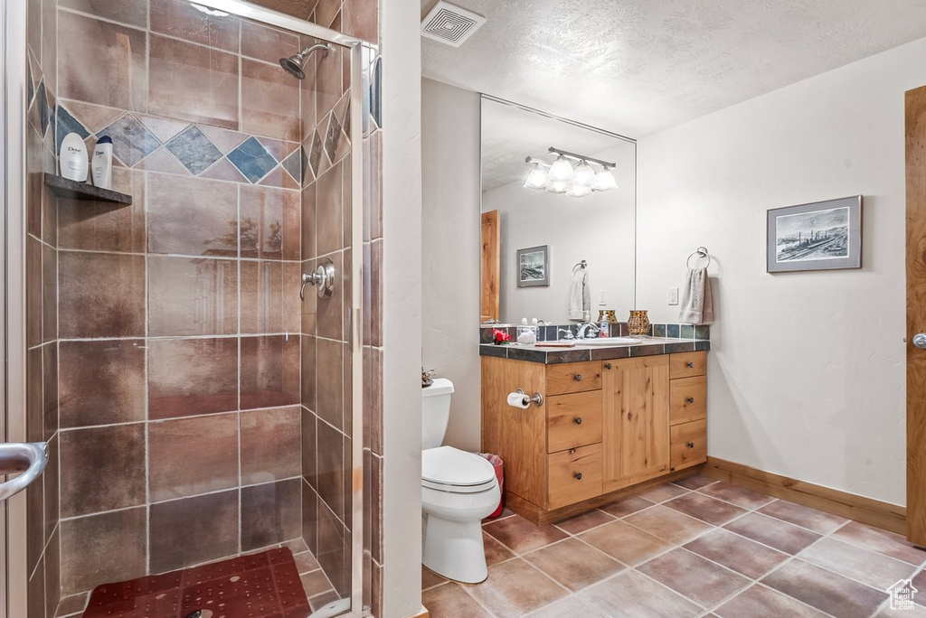 Bathroom with vanity, a tile shower, a textured ceiling, toilet, and tile flooring