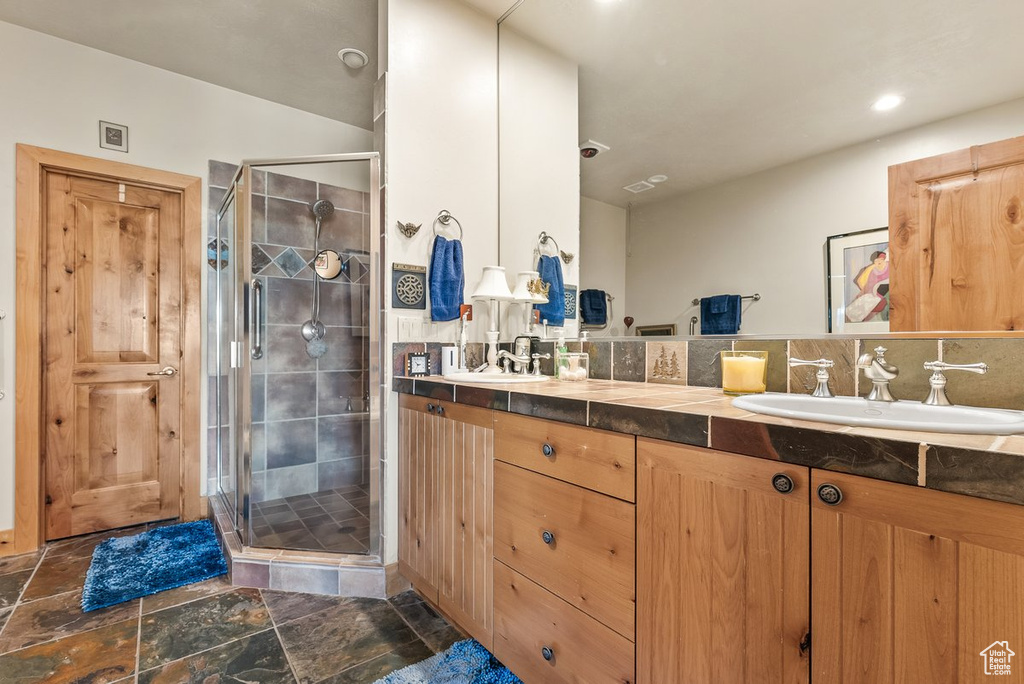 Bathroom featuring dual sinks, vanity with extensive cabinet space, tile flooring, and an enclosed shower