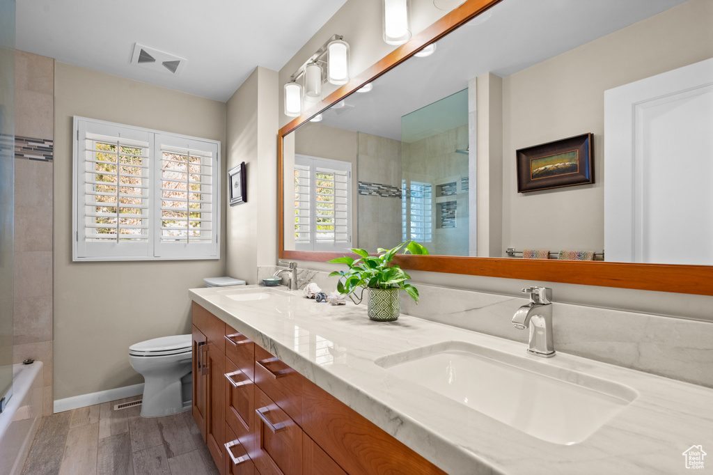 Full bathroom featuring tiled shower / bath, large vanity, dual sinks, toilet, and hardwood / wood-style floors