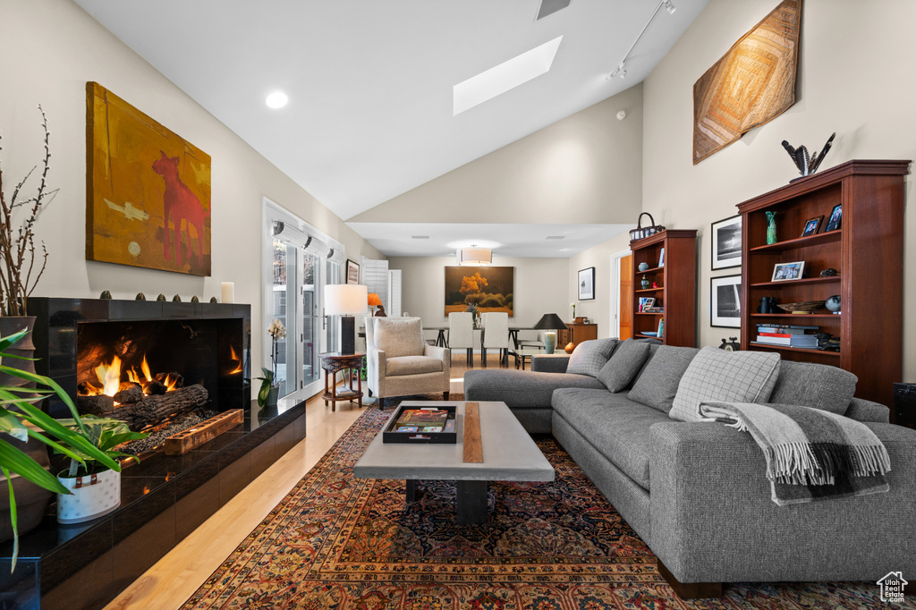 Living room featuring a tile fireplace, a skylight, high vaulted ceiling, and light hardwood / wood-style flooring