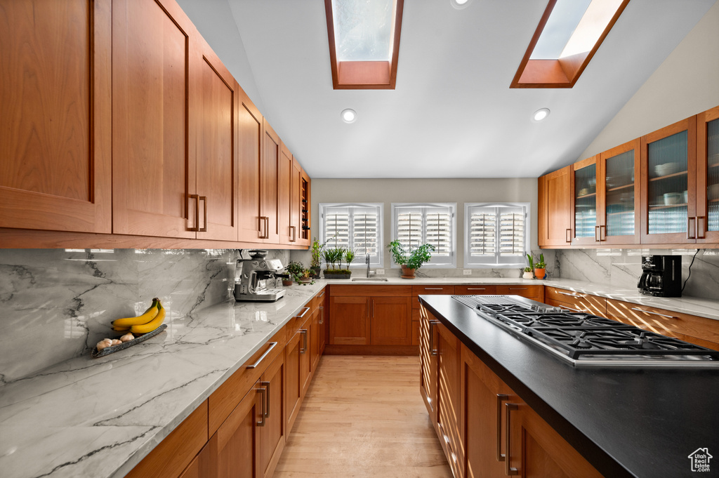 Kitchen with stainless steel gas cooktop, vaulted ceiling with skylight, light hardwood / wood-style flooring, and backsplash
