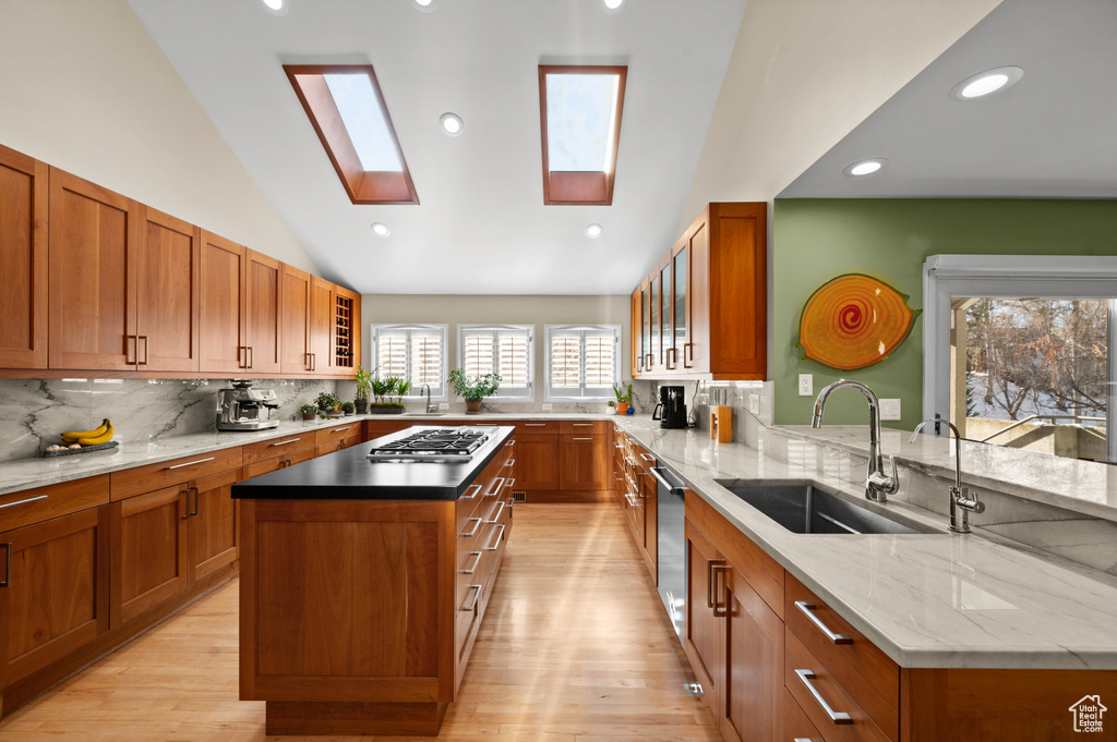 Kitchen with vaulted ceiling with skylight, light hardwood / wood-style floors, a center island, sink, and tasteful backsplash
