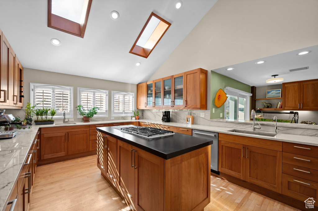 Kitchen featuring light wood-type flooring, a skylight, appliances with stainless steel finishes, sink, and a center island