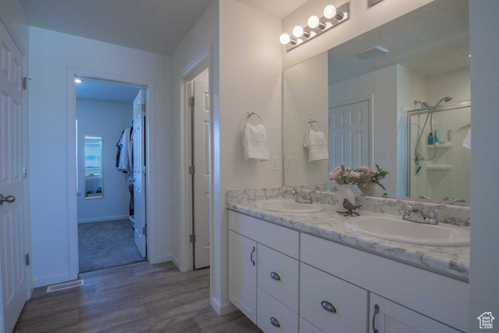 Bathroom featuring dual sinks, a shower with shower door, large vanity, and hardwood / wood-style flooring