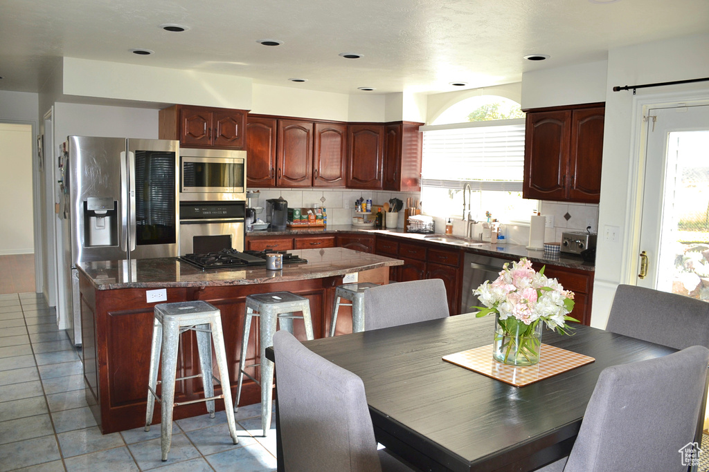 Kitchen with a kitchen island, light tile floors, tasteful backsplash, sink, and stainless steel appliances