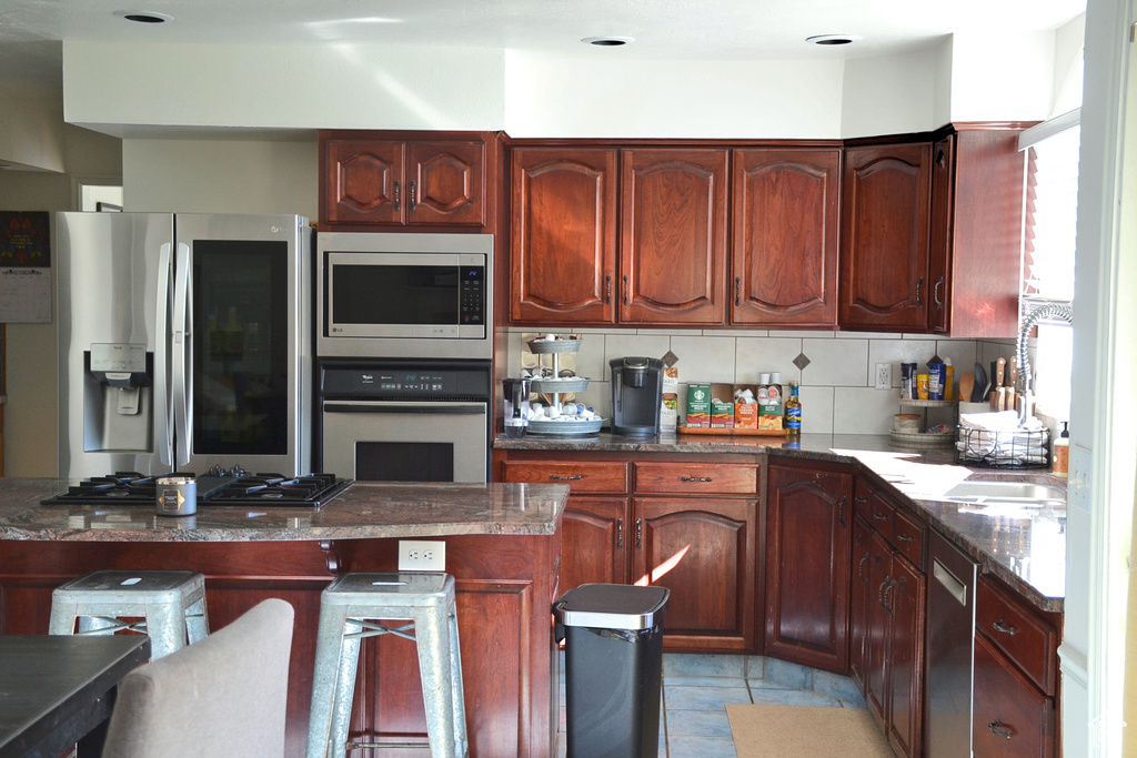 Kitchen featuring light tile flooring, dark stone counters, a kitchen bar, stainless steel appliances, and backsplash