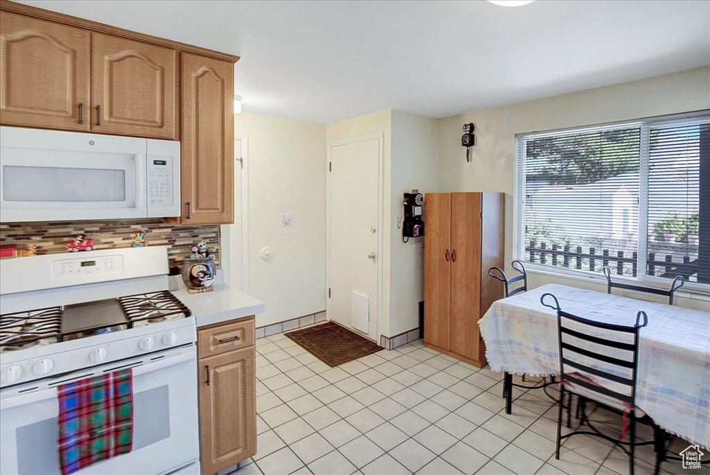 Kitchen with backsplash, white appliances, and light tile flooring