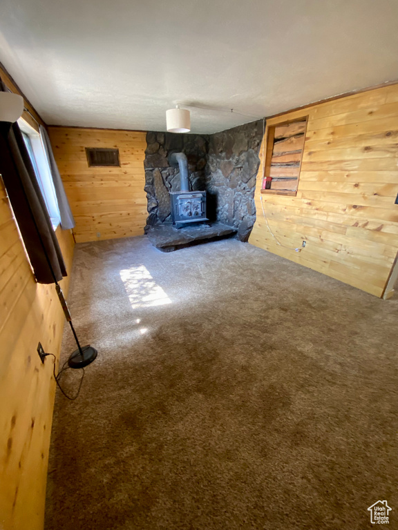 Unfurnished living room with wooden walls, carpet flooring, and a wood stove