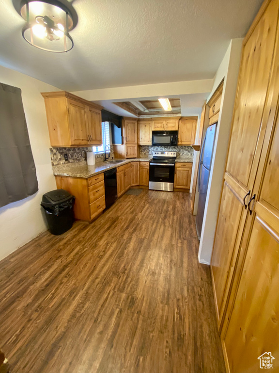 Kitchen featuring dark hardwood / wood-style flooring, black appliances, light stone counters, sink, and tasteful backsplash