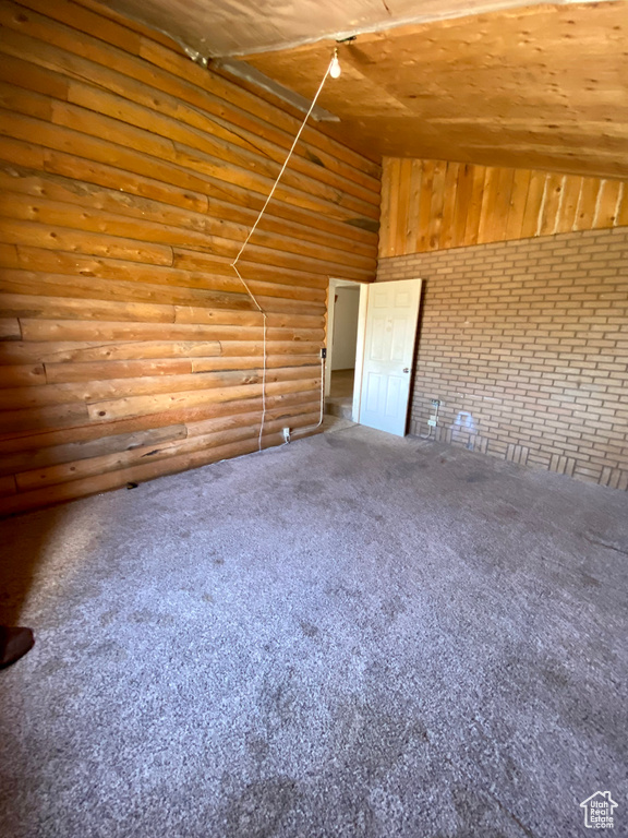 Unfurnished room featuring rustic walls, carpet flooring, wooden ceiling, and lofted ceiling