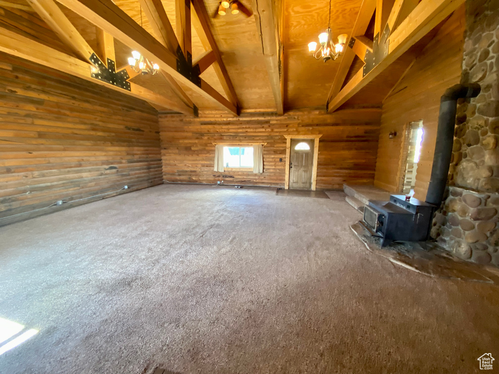 Carpeted spare room with a wood stove, wood ceiling, a chandelier, high vaulted ceiling, and beamed ceiling