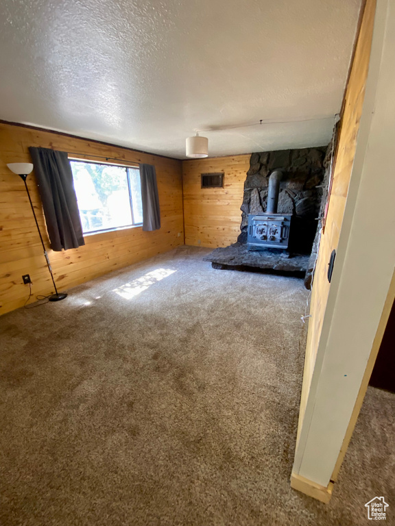 Unfurnished living room with a wood stove, carpet floors, wooden walls, and a textured ceiling