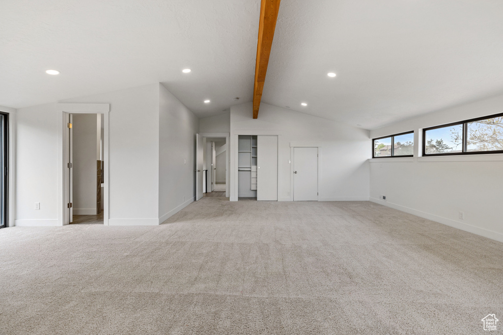 Unfurnished living room featuring light colored carpet and lofted ceiling with beams