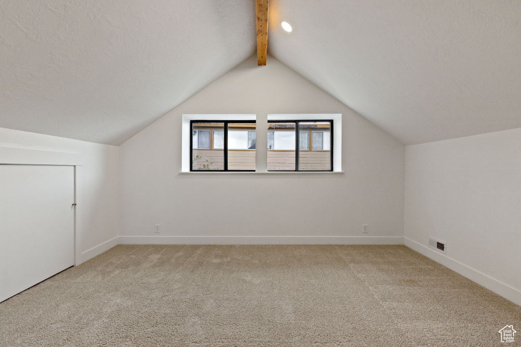 Additional living space with a textured ceiling, carpet floors, and vaulted ceiling with beams